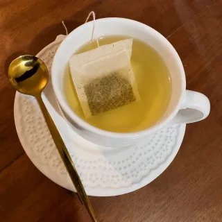 Chá de erva-doce Afeto do Campo, servido em xícara branca com sachê de ervas e colher dourada sobre mesa de madeira, em apresentação delicada e acolhedora.